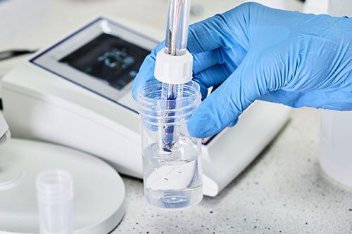 GettyImages-1265061681-copy A person holding a tube of liquid in front of a scale.