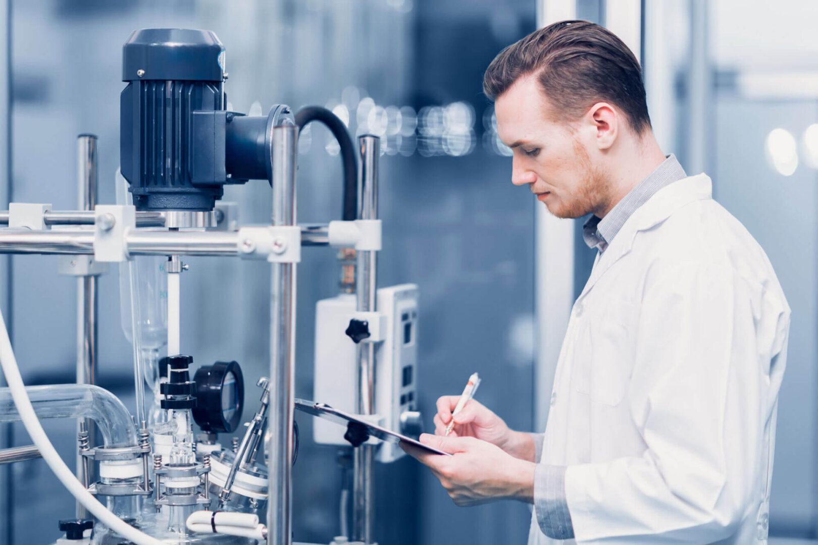 A man in lab coat writing on paper next to machine.