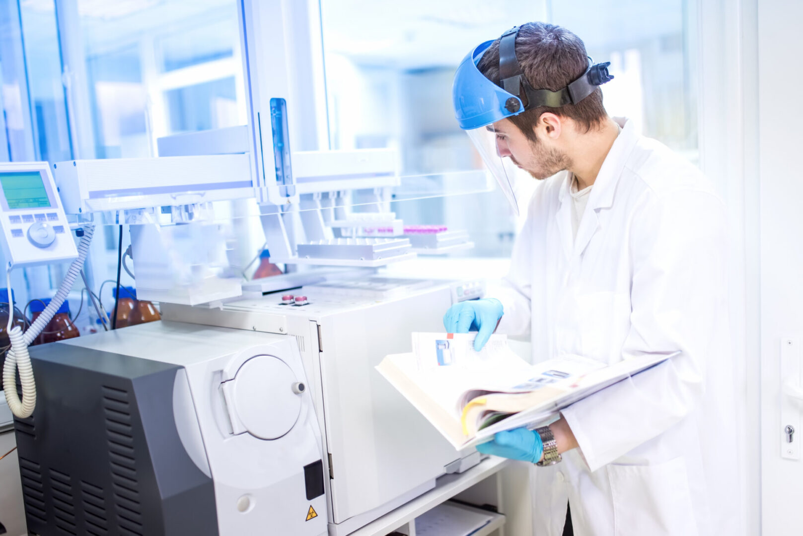 Scientist using manual for programming a chemical computer machinery A man in lab coat and goggles holding papers.