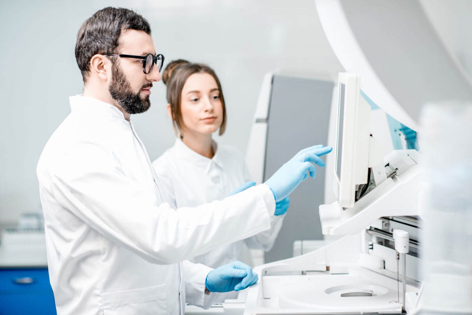 Two people in lab coats and gloves looking at a computer.