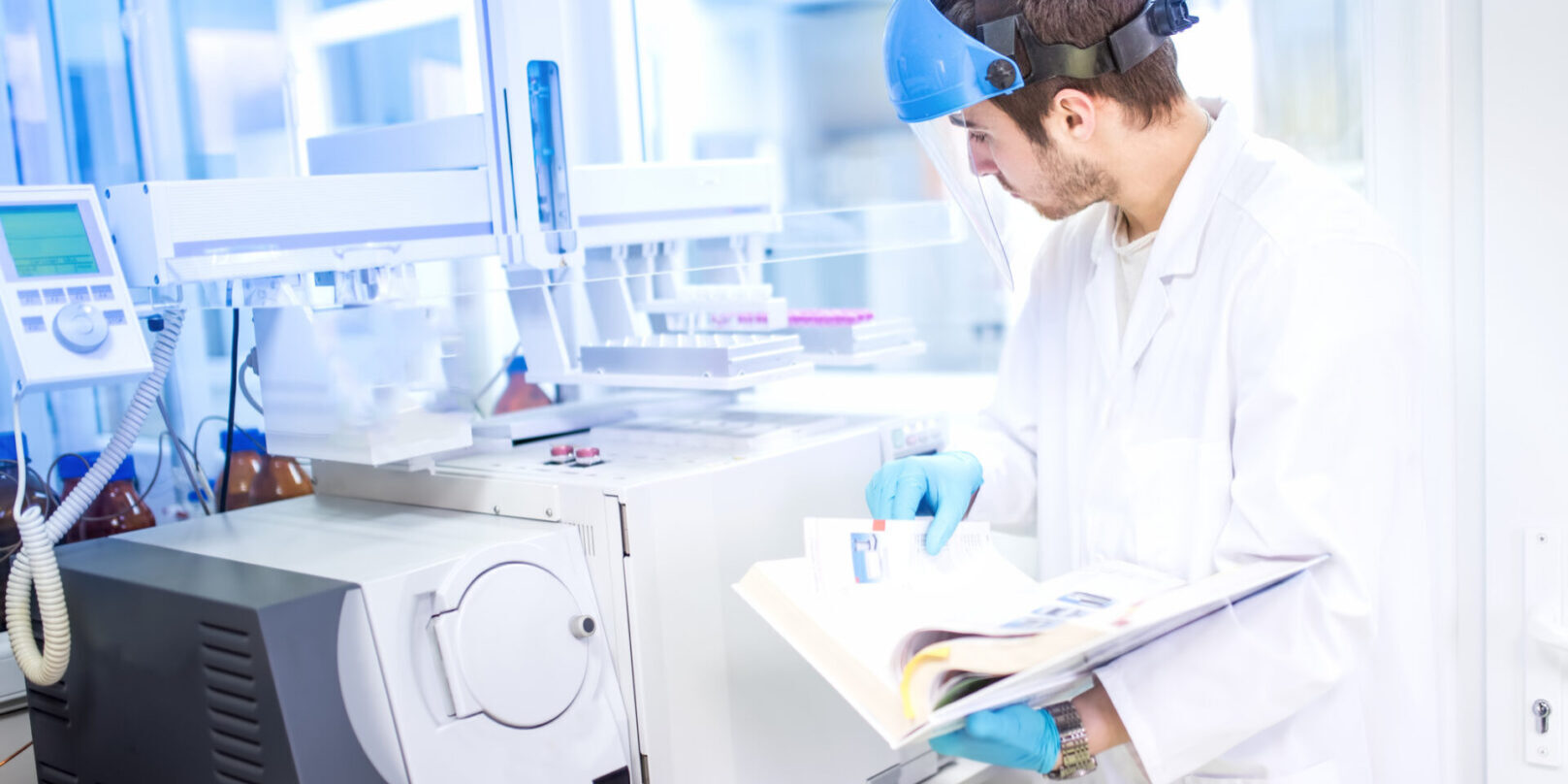 Scientist using manual for programming a chemical computer machinery A man in lab coat and goggles holding papers.